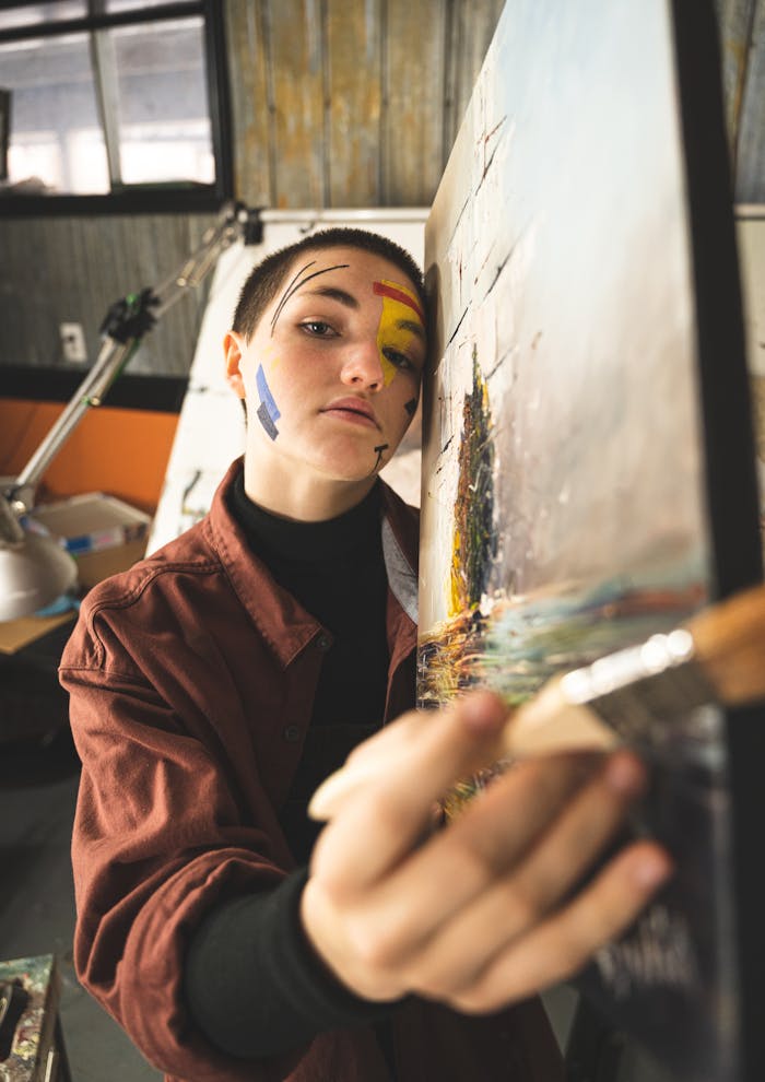Artist with face paint working on a painting in a studio setting.