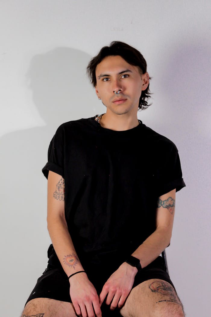 The Art of Drawing Readers In: Your attractive post title goes here Studio portrait of a young man in black attire with tattoos and a septum piercing on a white background.