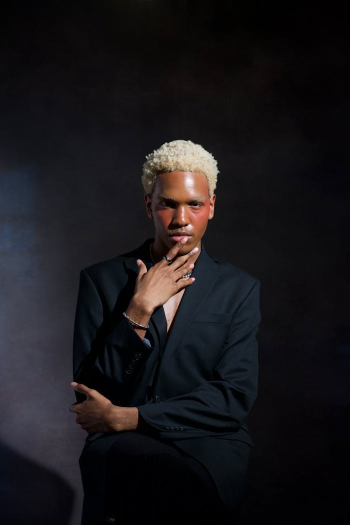 contact-img Fashion portrait of a model in a black suit with dyed hair against a dark background.