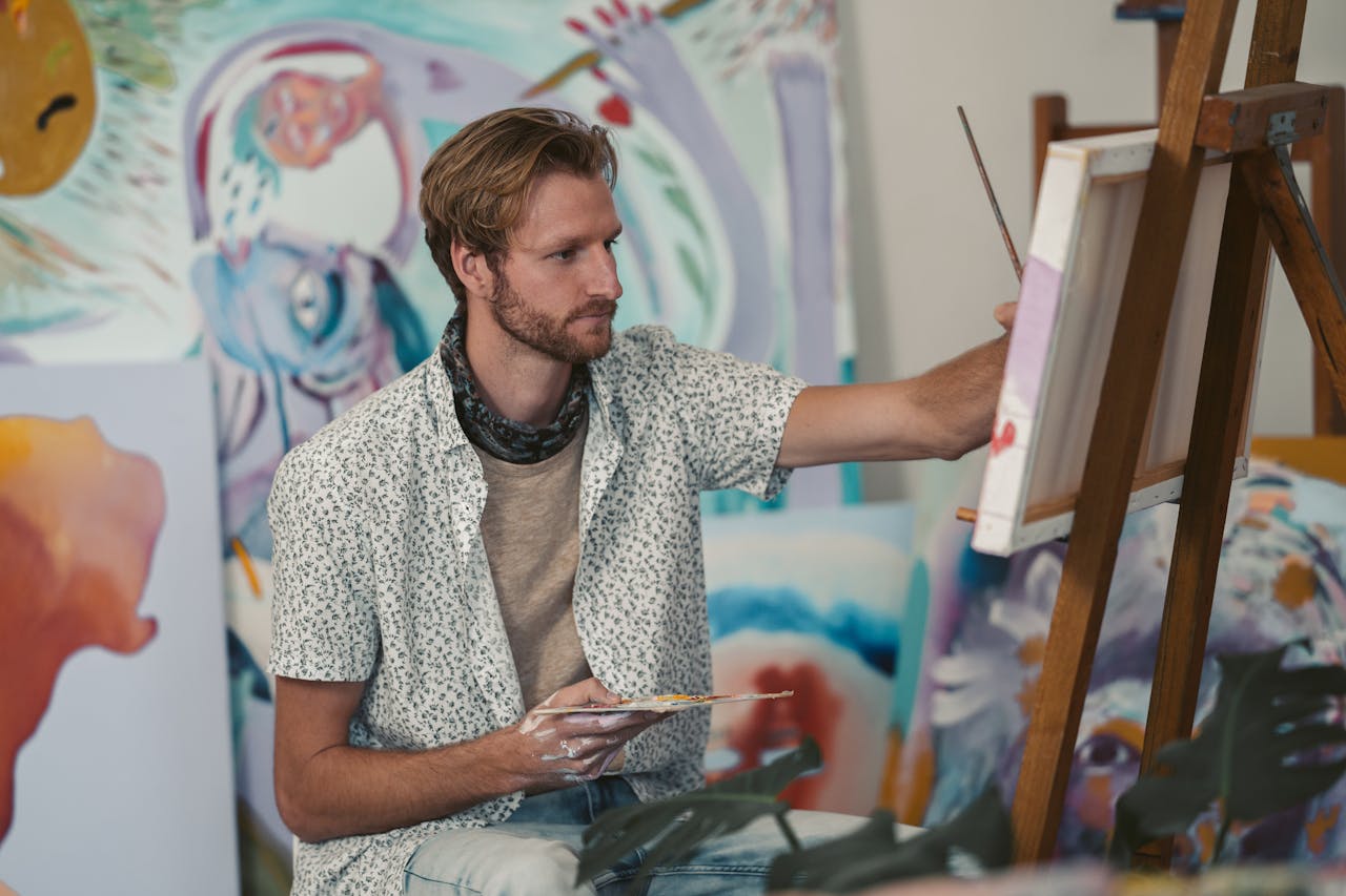 Crafting Captivating Headlines: Your awesome post title goes here Bearded male artist painting on canvas in a vibrant studio setting, surrounded by artwork.