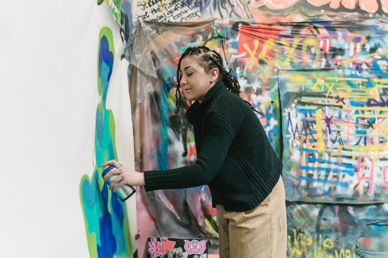 Woman artist spray painting a colorful mural indoors, expressing creativity.