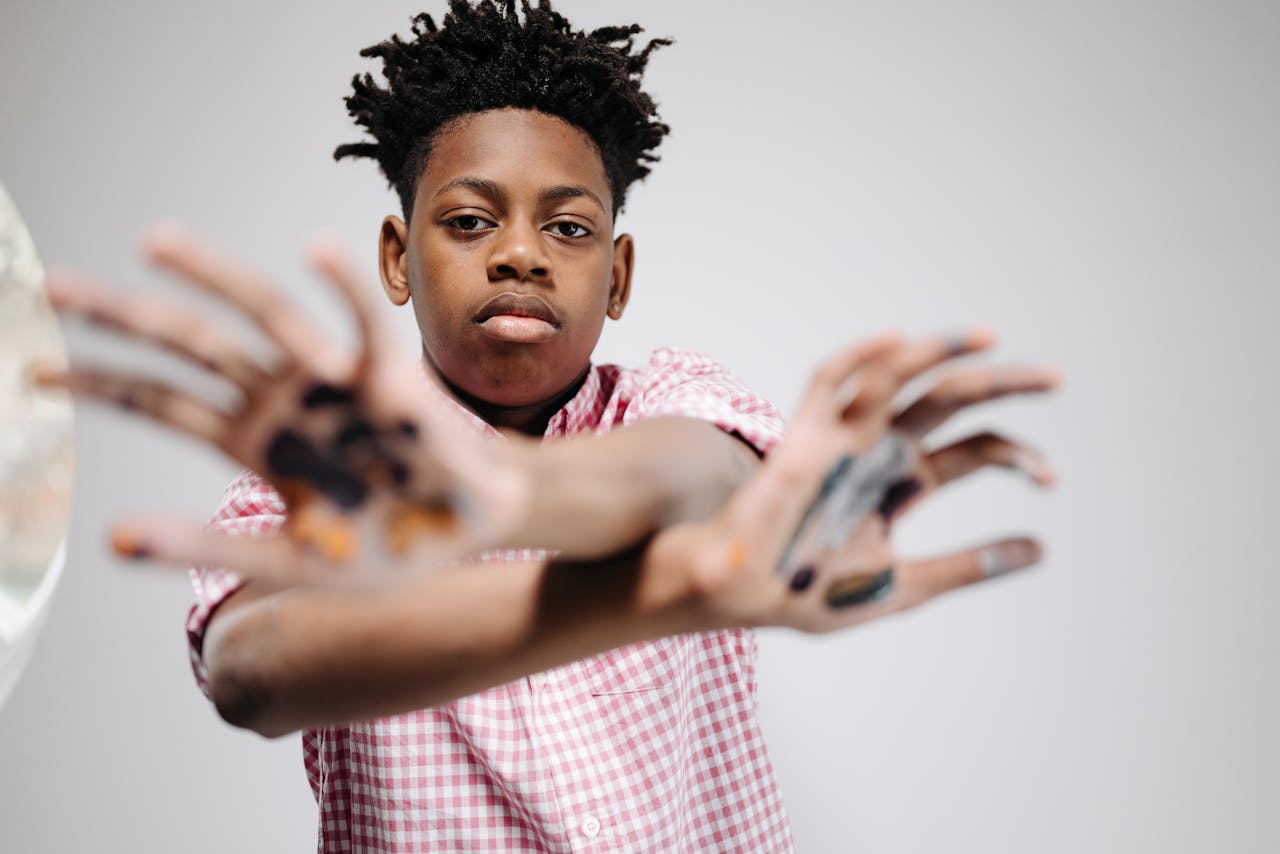 A young boy shows his painted hands, expressing creativity and artistry in a studio shoot.