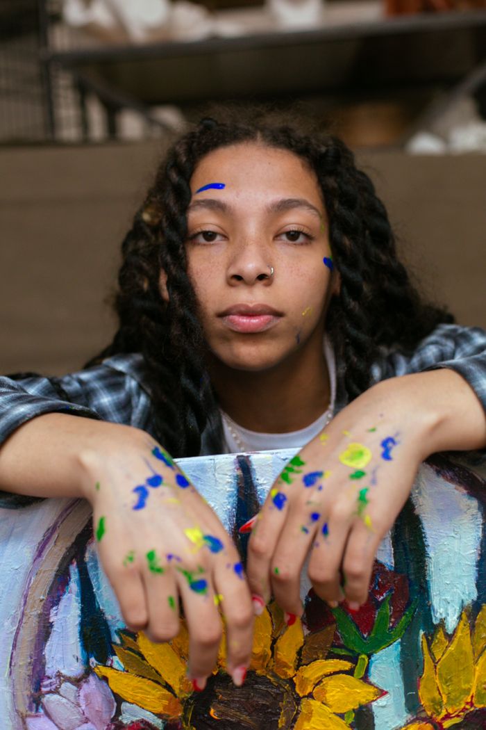 Creative young artist posing with hands covered in vibrant paint, showcasing artwork with sunflower motif.